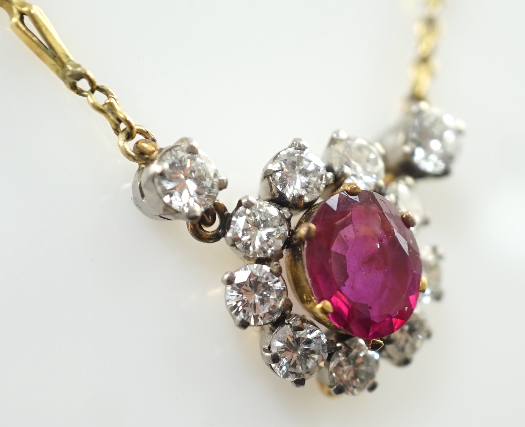 A modern 9ct gold, single stone oval cut ruby and eleven stone round cut diamond cluster set pendant necklace